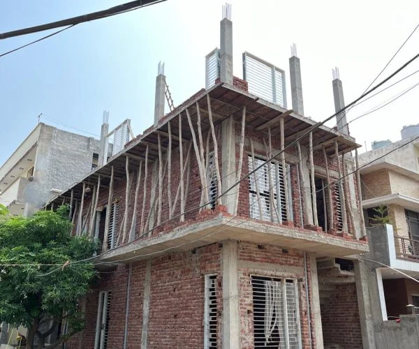 Three-storey residential building under construction in kharar with exposed brick walls, concrete columns, and temporary wooden scaffolding in a suburban neighborhood.